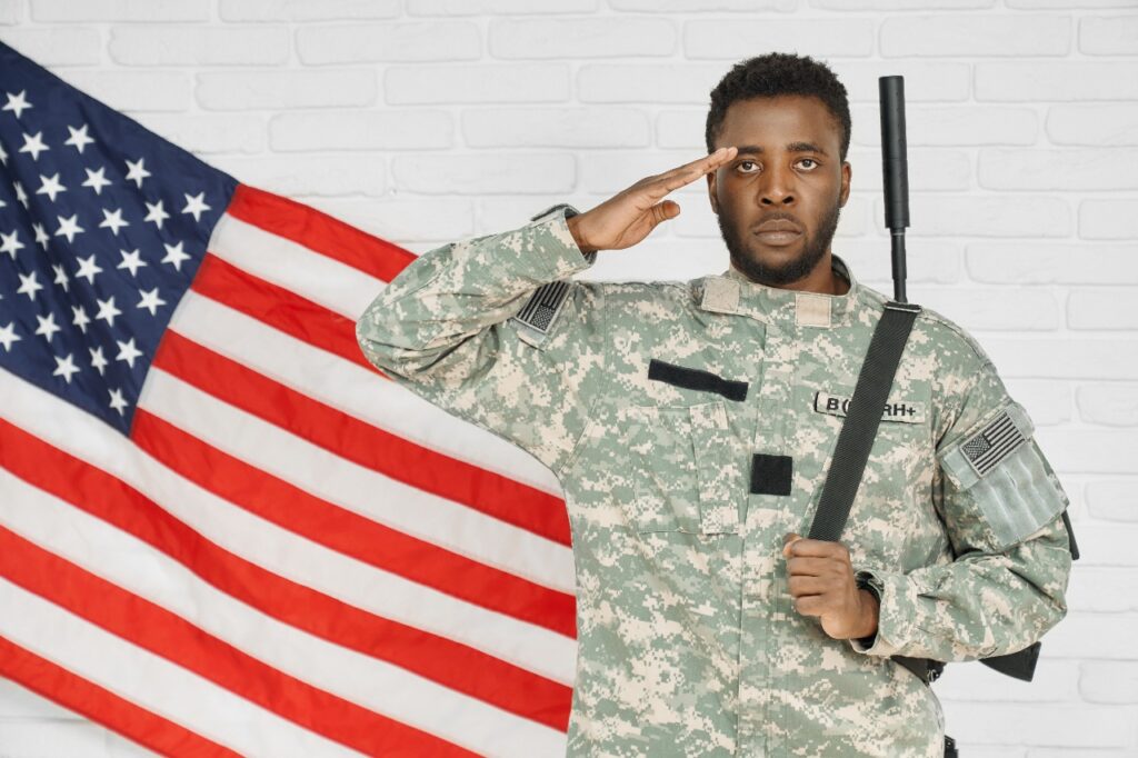 A male soldier in military uniform saluting while standing in front of the American flag, symbolizing patriotism and service.