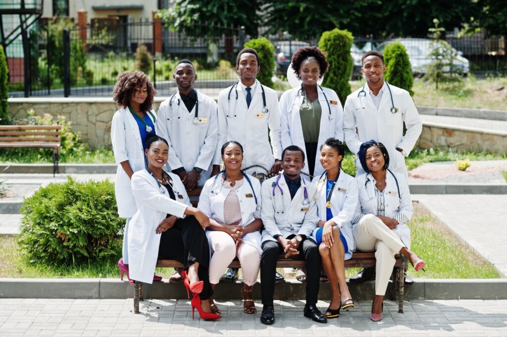 Group of nine Kenyan healthcare professionals wearing white medical coats and stethoscopes, posed outdoors in a green campus courtyard, symbolizing teamwork, diversity, and dedication in medicine.