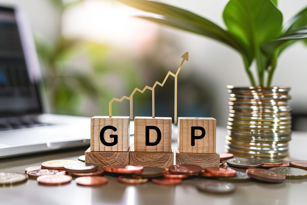Wooden blocks spelling GDP with coins, a small plant, and an upward arrow graph symbolizing economic growth.
