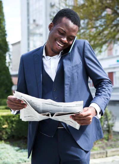 A man in a suit and tie smiles while holding a newspaper